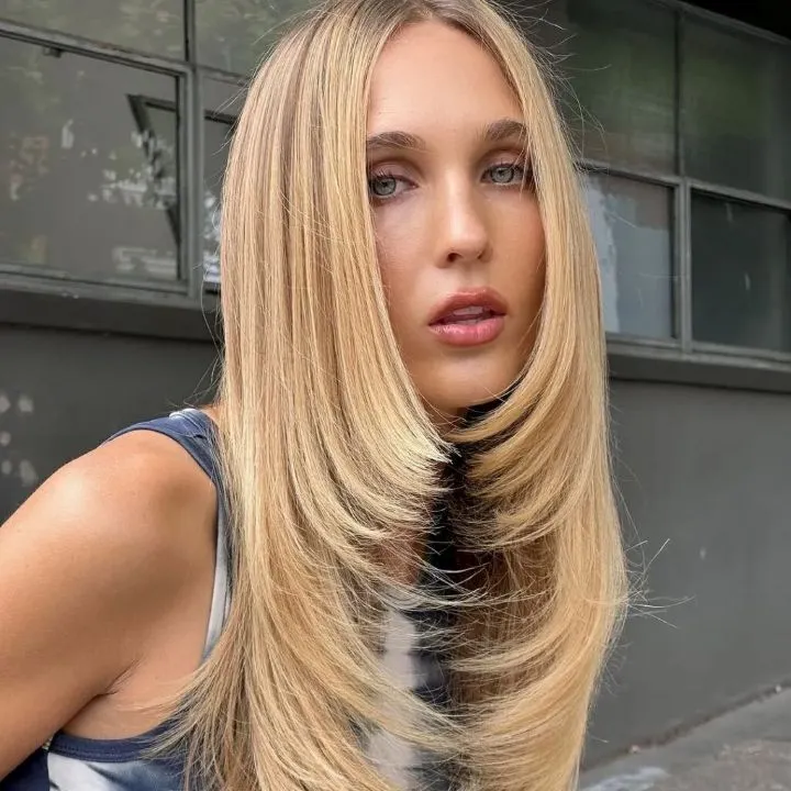 A blonde woman with a straight step-cut hairstyle.