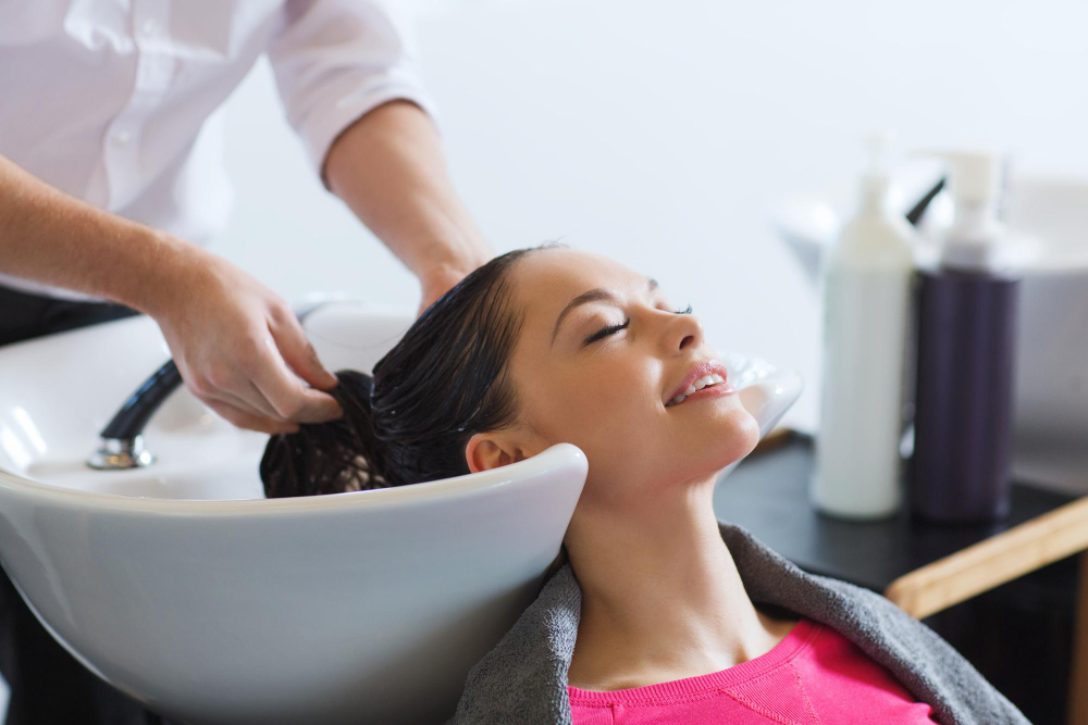 happy young woman with hairdresser washing head at hair salon - benefits of hair spa
